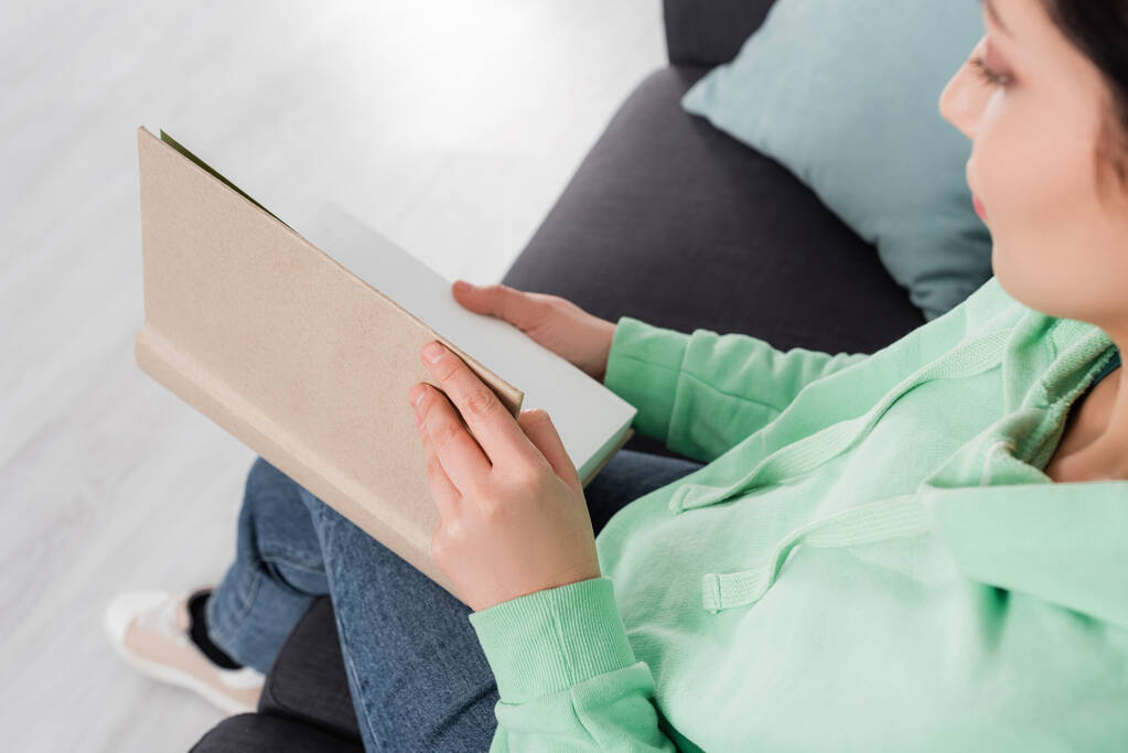 Высокий угол зрения размытой женщины, читающей книгу в гостиной  - Фото, изображение