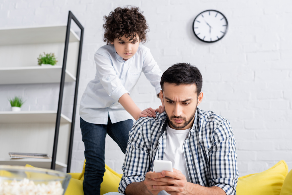 Arabisches Kind schaut sich zu Hause ernste Vater-Nachrichten auf Smartphone an - Foto, Bild