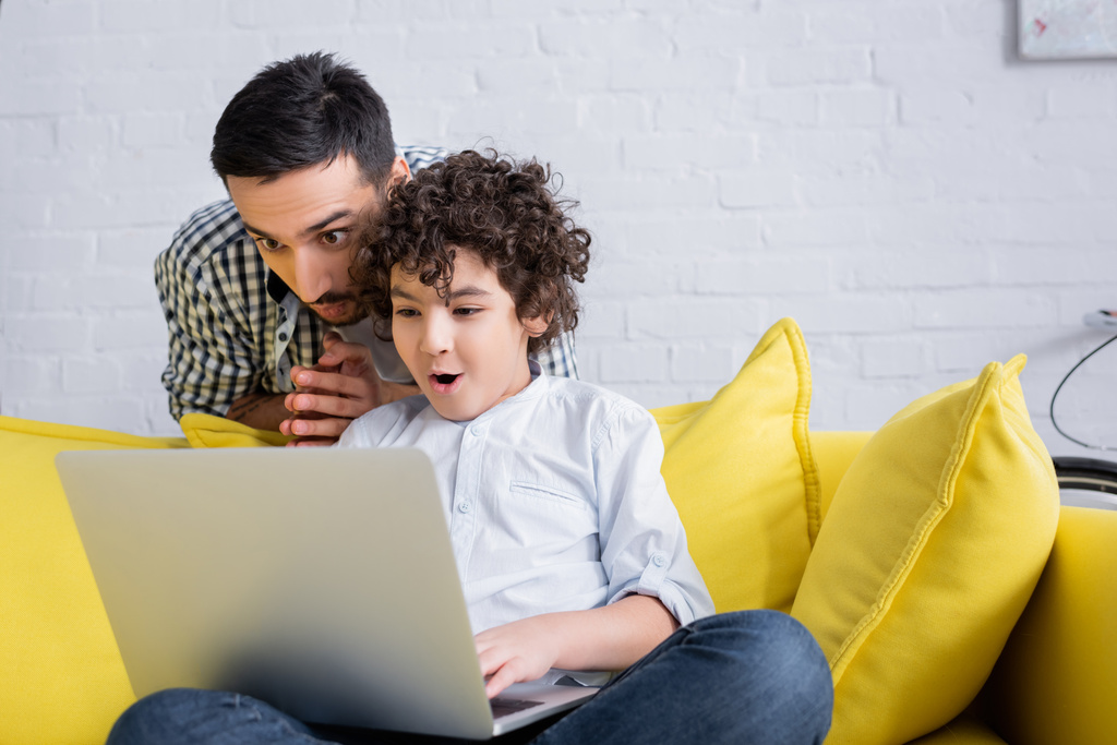 elképedt arab fiú használ laptop közelében apa otthon - Fotó, kép