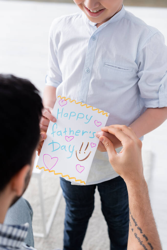 cropped view of smiling kid holding happy fathers day card near dad on blurred foreground - Photo, Image