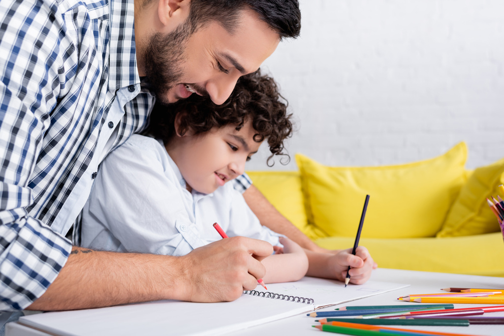 cheerful muslim father and son drawing in sketchbook with pencils - Photo, Image