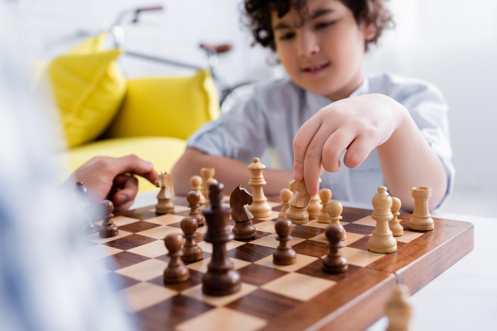 enfoque selectivo de tablero de ajedrez cerca de niño musulmán y padre jugando en casa - Foto, imagen