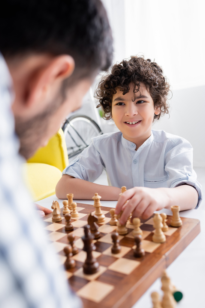 sorridente ragazzo arabo giocare a scacchi con papà in primo piano sfocato - Foto, immagini