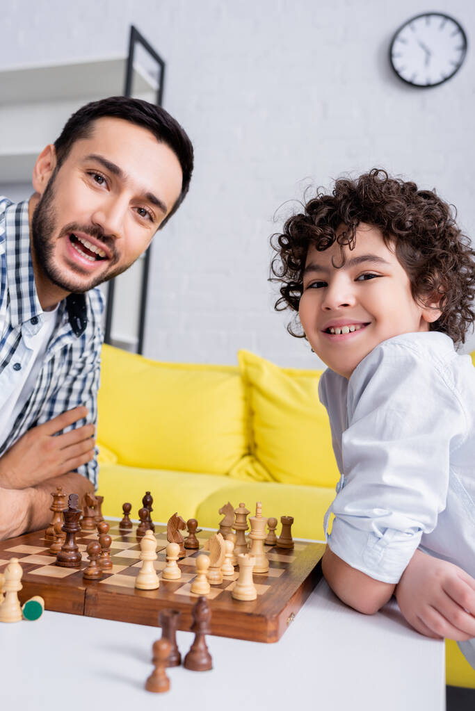 Gelukkig moslim vader en kind kijkend naar camera nabij schaken op wazige voorgrond  - Foto, afbeelding