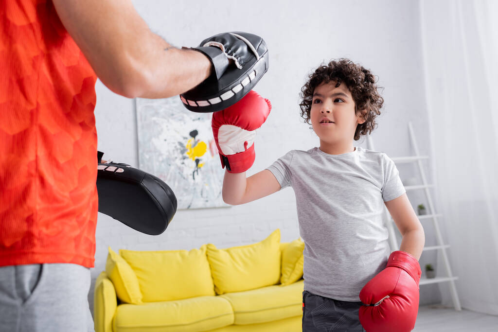 Padre en guantes de ponche de pie cerca de hijo musulmán en guantes de boxeo en casa  - Foto, Imagen