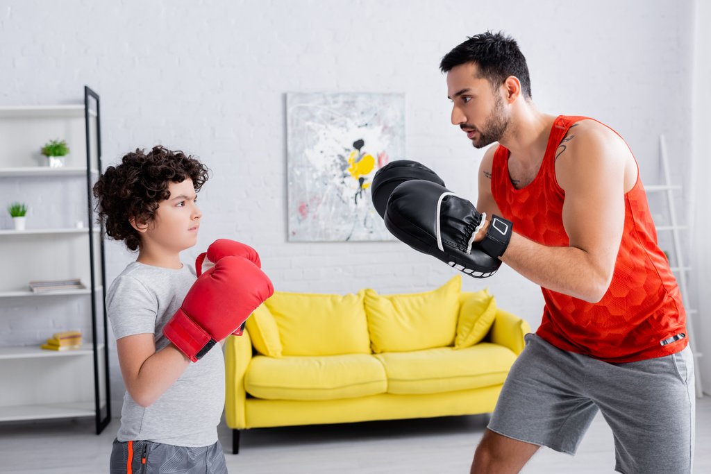 Мусульманский сын в боксёрских перчатках тренируется с отцом дома  - Фото, изображение