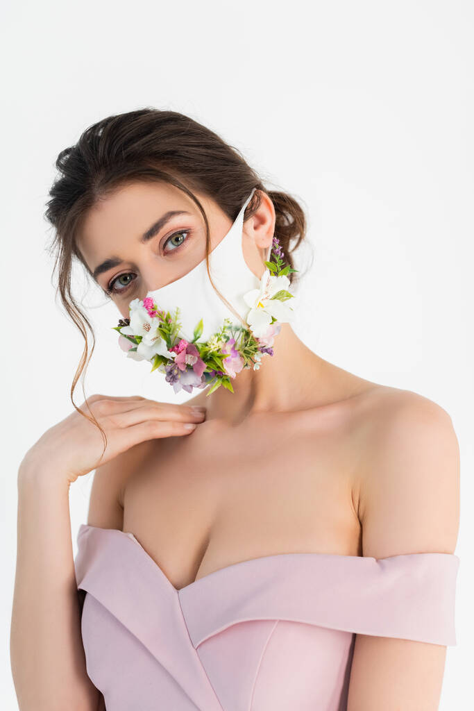 jonge vrouw, het dragen van medische masker met bloemen, kijken naar camera geïsoleerd op wit - Foto, afbeelding