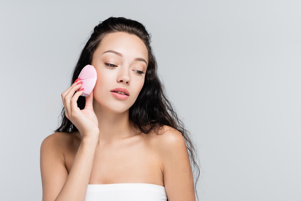 brunette young woman using cleansing brush isolated on grey - Photo, Image