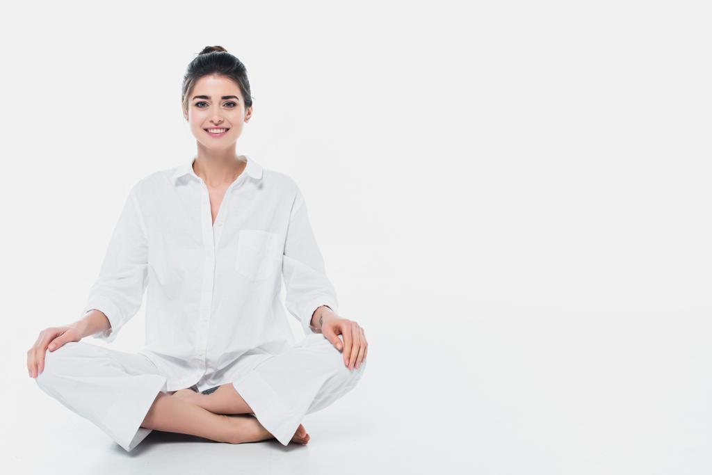 Vrolijke vrouw zitten in yoga pose en glimlachen op camera op witte achtergrond  - Foto, afbeelding