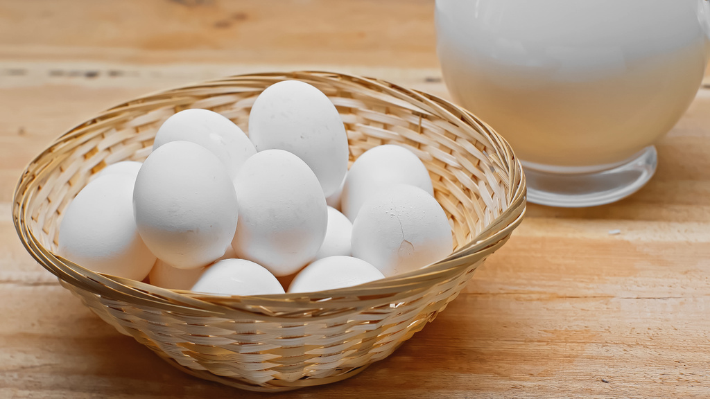 cesta de mimbre con huevos blancos cerca de frasco de vidrio con leche fresca en la superficie de madera - Foto, imagen