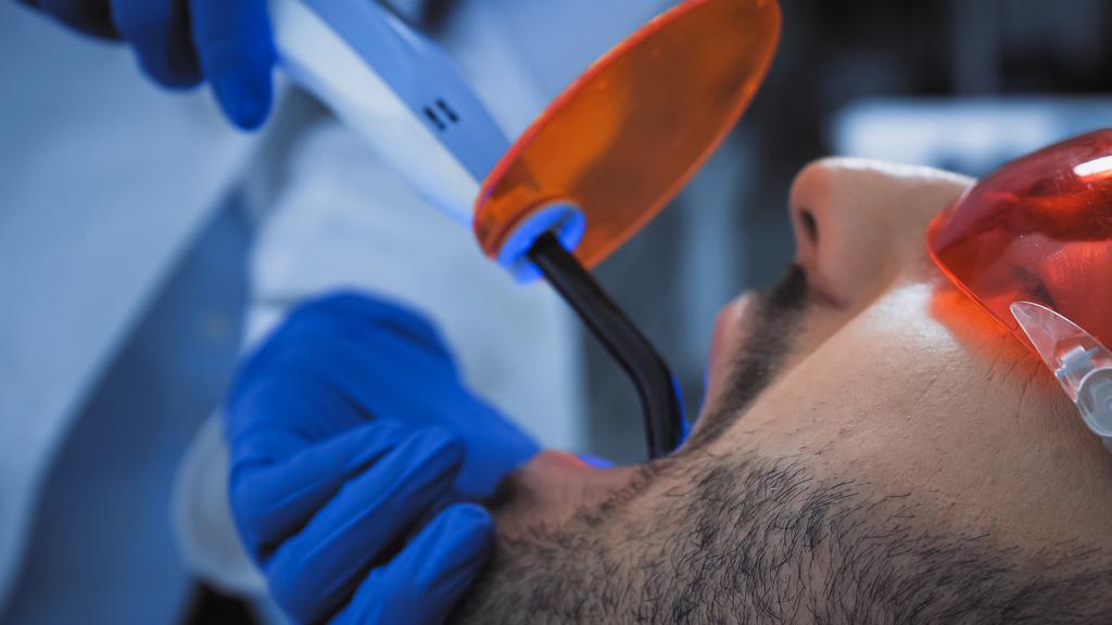levágott kilátás a fogorvos gazdaság ultraibolya lámpa közelében beteg - Fotó, kép