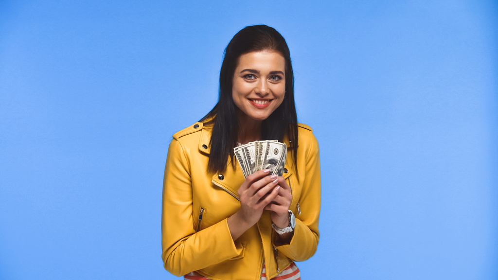 Vidám fiatal nő kezében dollár bankjegyek elszigetelt kék - Fotó, kép