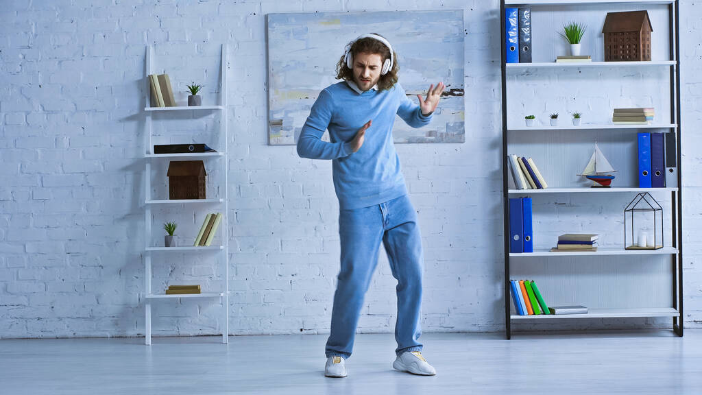 visão completa do jovem empresário em fones de ouvido sem fio dançando no escritório moderno - Foto, Imagem