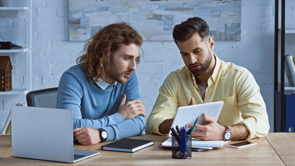молодые бизнесмены смотрят на цифровой планшет во время обсуждения в офисе - Фото, изображение