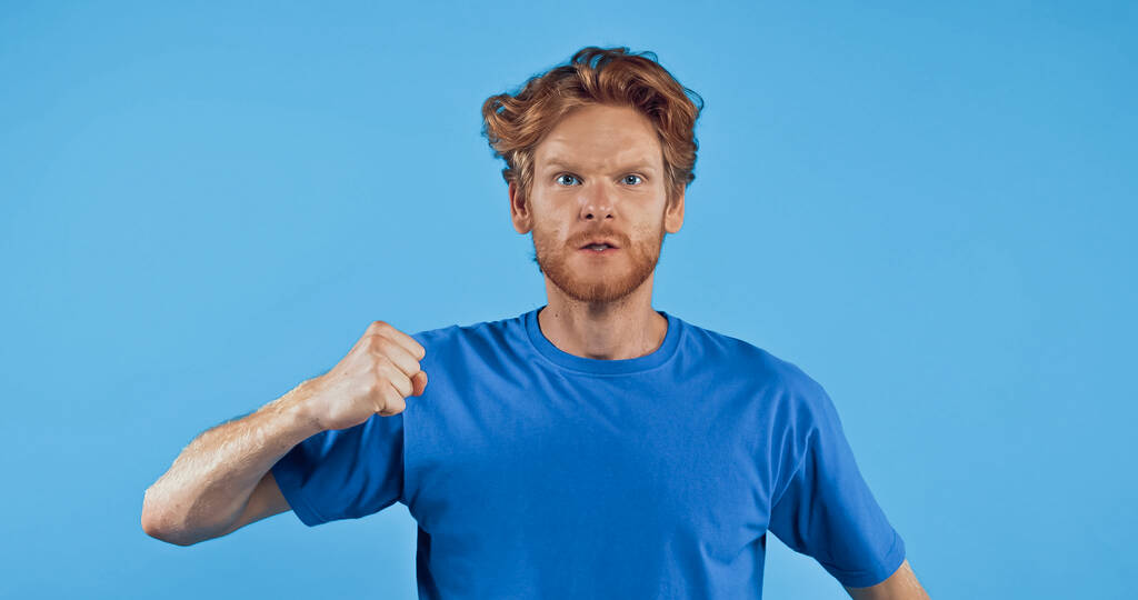 сердитий рудий чоловік показує згорнутий кулак ізольований на синьому
 - Фото, зображення