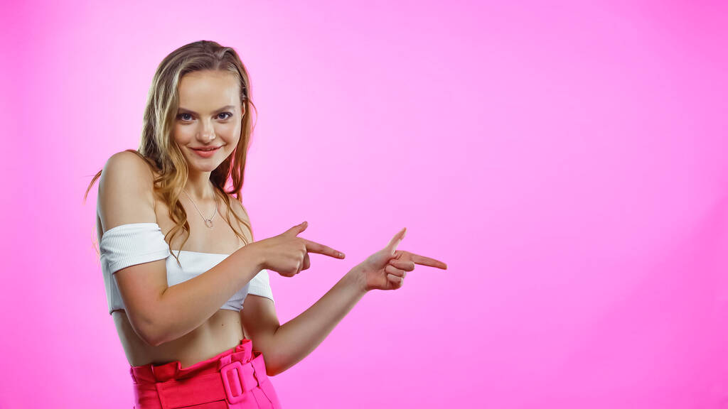 jonge vrouw in gewas top wijzend met vingers op roze - Foto, afbeelding