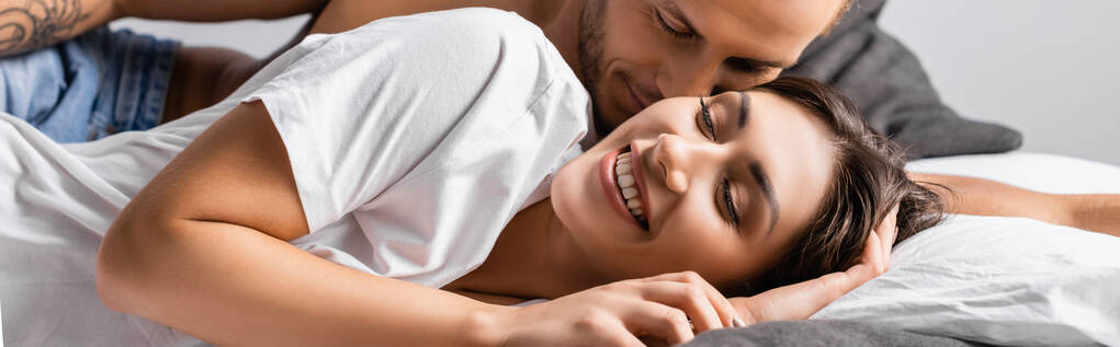 Bezkoszulowy mężczyzna całujący uśmiechniętą dziewczynę na łóżku, baner  - Zdjęcie, obraz