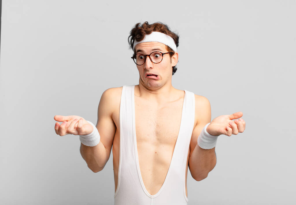 humorous sport man shrugging with a dumb, crazy, confused, puzzled expression, feeling annoyed and clueless - 写真・画像
