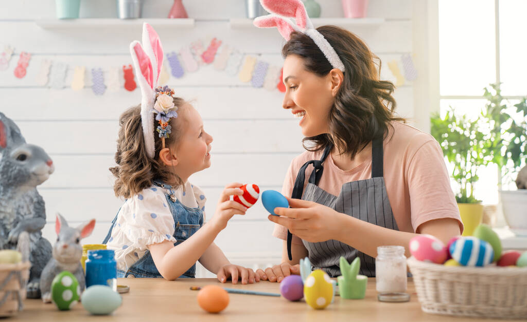 Anya és lánya tojást festenek. Boldog család készül húsvétkor. Aranyos kislány visel nyuszifül. - Fotó, kép