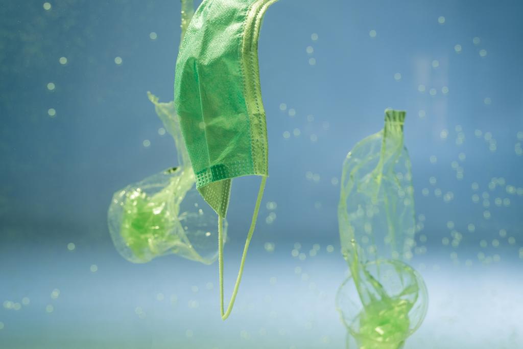 Suda kullanılan tıbbi maskenin yanında plastik torbalar ve fincanlar, ekoloji konsepti - Fotoğraf, Görsel
