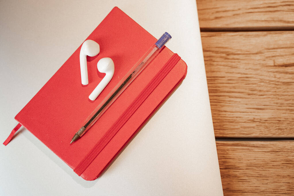 vista superior de auriculares inalámbricos en cuaderno rojo con pluma  - Foto, Imagen