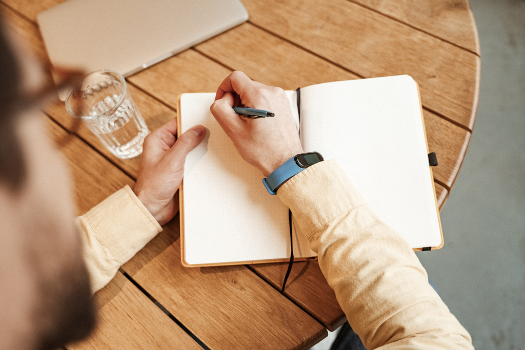 hoge hoek uitzicht van freelancer met slimme horloge op de hand schrijven in notebook  - Foto, afbeelding