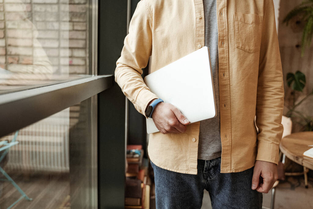 cropped view of freelancer holding laptop while standing near window - Photo, Image