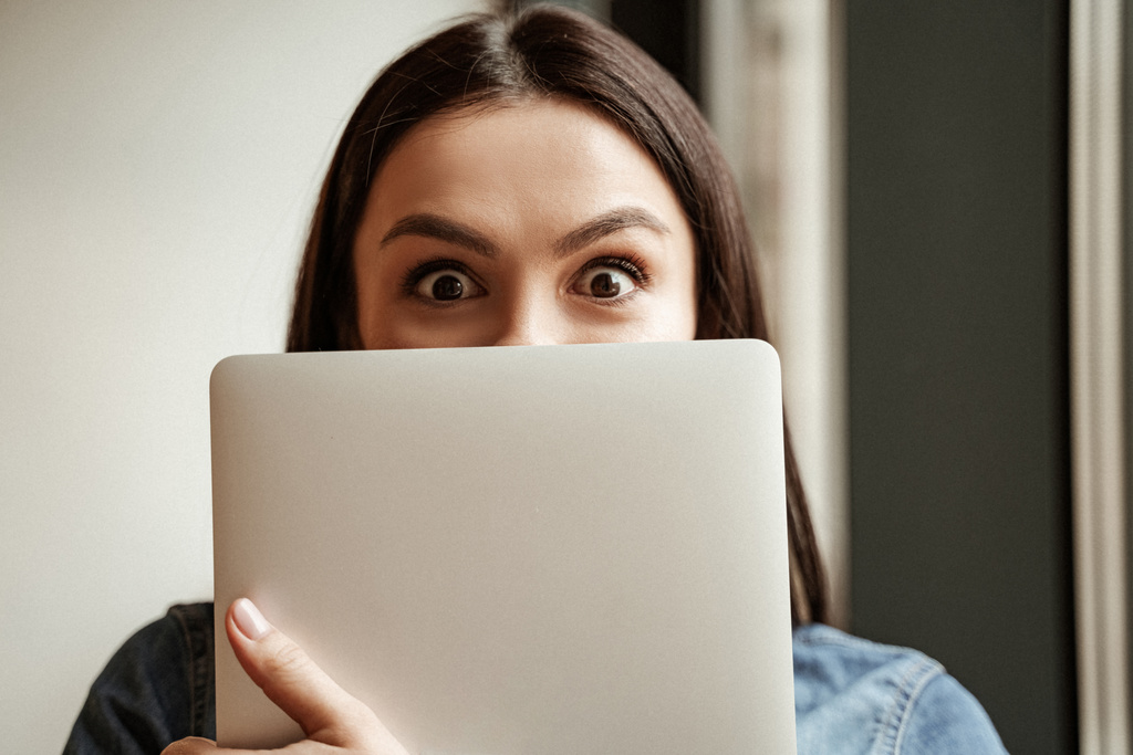 freelancer pokrycie twarzy podczas trzymania laptopa i patrząc w kamerę - Zdjęcie, obraz