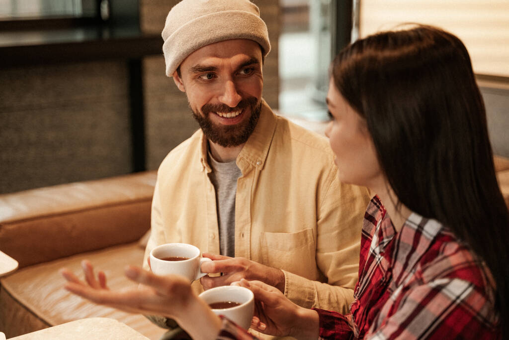 man met baard in muts hoed met kopje koffie en het nemen met vrouw op wazig voorgrond - Foto, afbeelding