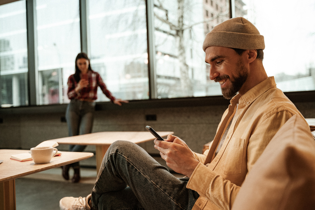 vrolijk man sms 'en op smartphone terwijl zitten op de bank in cafe - Foto, afbeelding