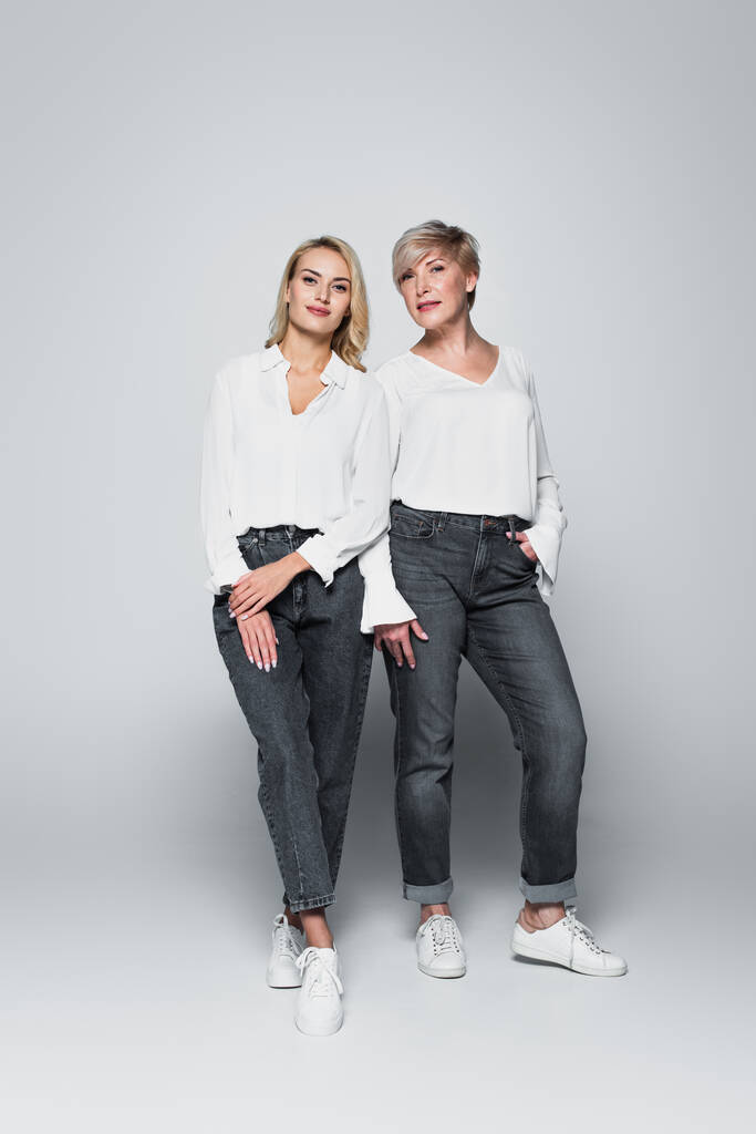full length view of fashionable mother and daughter looking at camera while posing on grey - Zdjęcie, obraz