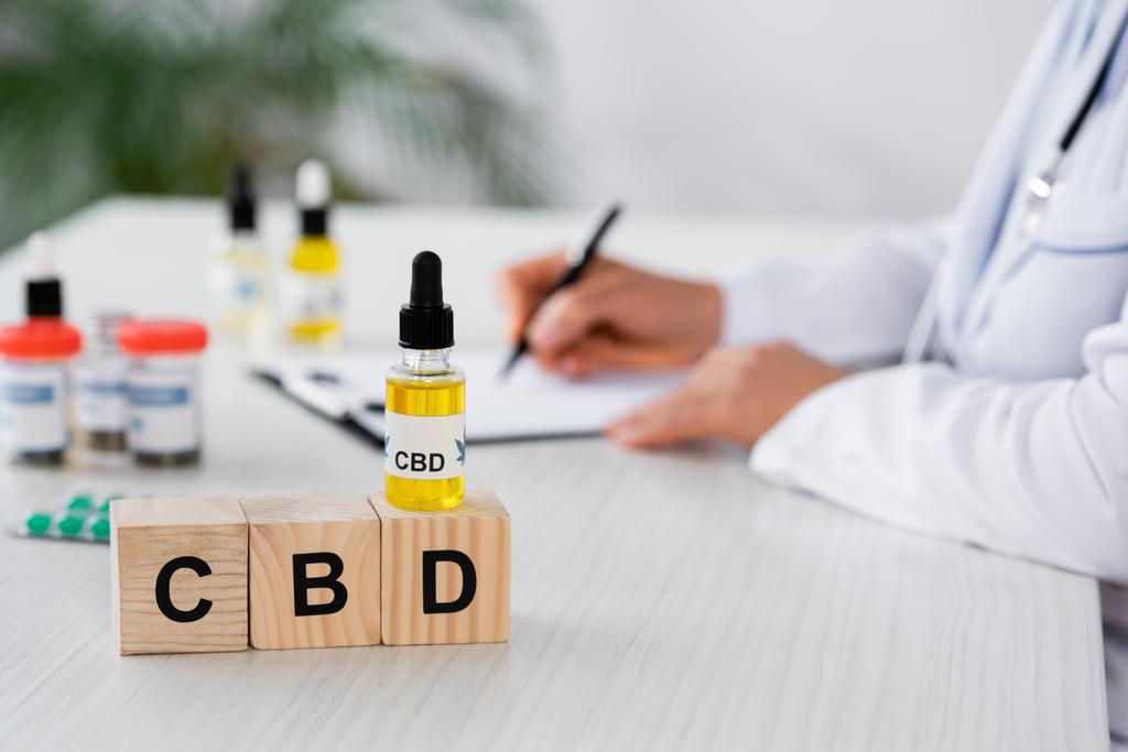 обрезанный вид врача, выписывающего рецепт рядом с кубиками CBD и лекарствами на столе - Фото, изображение