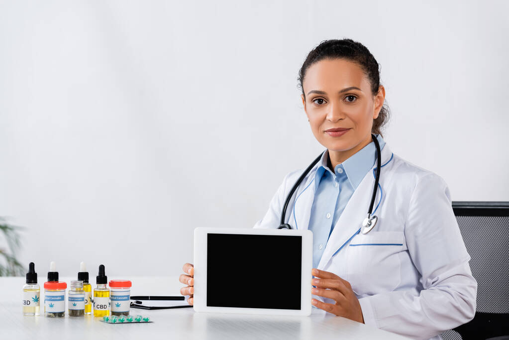 Afrikai amerikai orvos gazdaság digitális tabletta üres képernyőn közelében cbd gyógyszert az asztalon - Fotó, kép