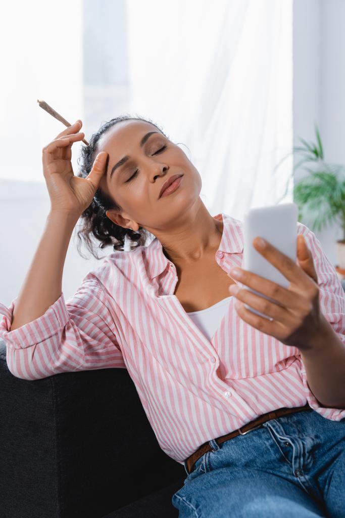 donna afro-americana in possesso di giunto laminato con cannabis medica e smartphone - Foto, immagini
