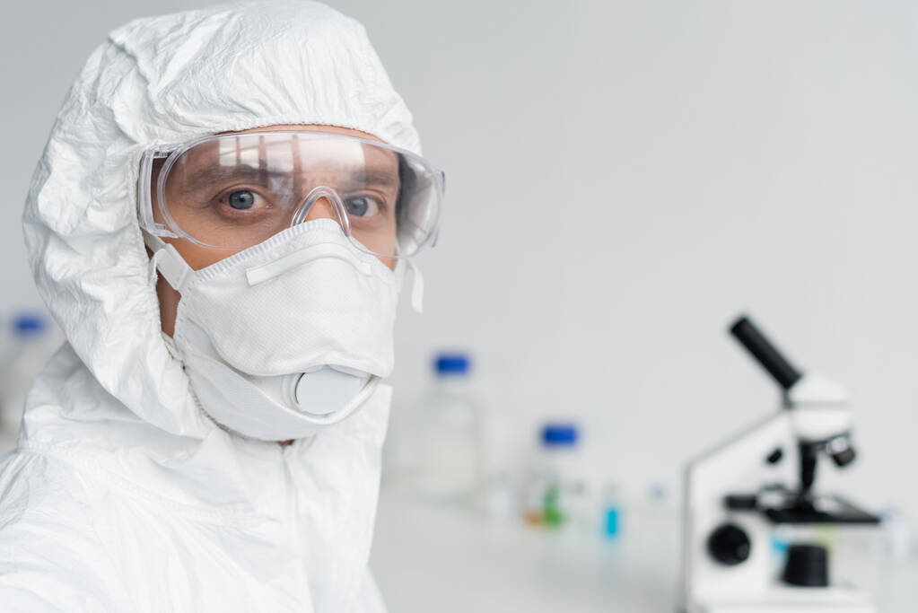 Scientist in goggles and hazmat suit looking at camera in laboratory  - Photo, Image