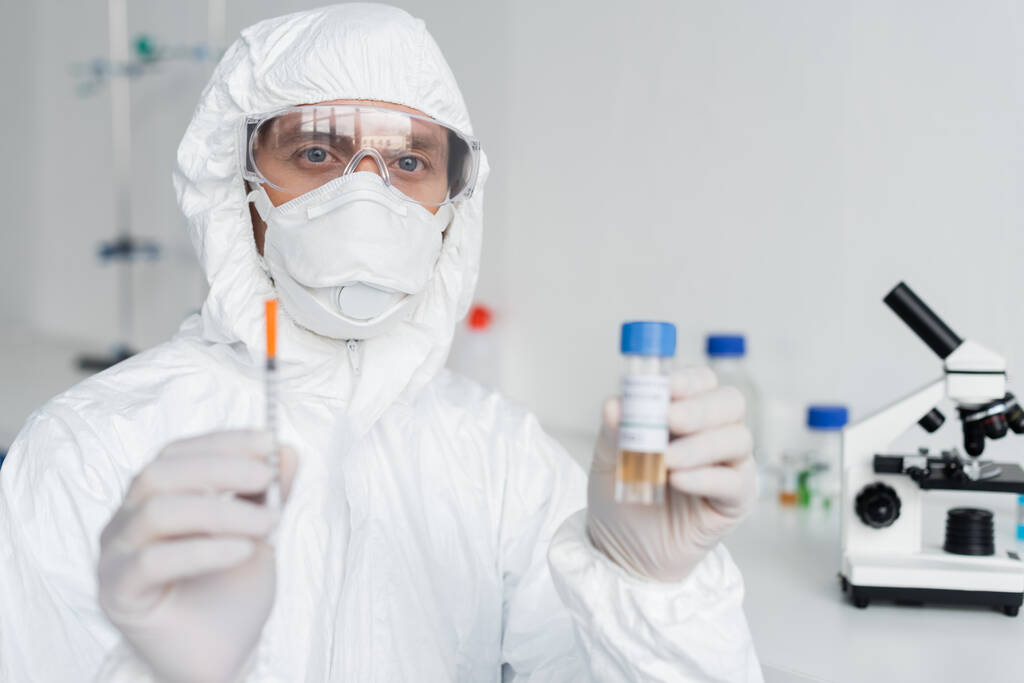 Scientist holding syringe and vaccine on blurred foreground in laboratory  - Φωτογραφία, εικόνα