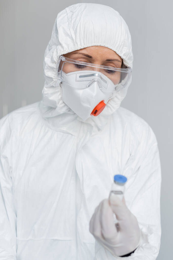 Suojalaseissa ja suojapuvuissa oleva tutkija, joka pitää rokotetta hämärtyneessä etualalla  - Valokuva, kuva