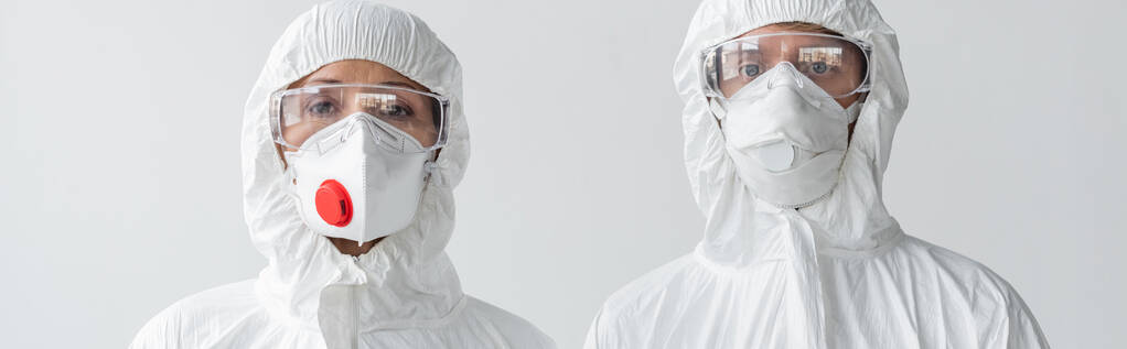 Naukowcy w kombinezonach ochronnych i maskach patrzący na kamerę odizolowaną na szarym, szarym transparencie  - Zdjęcie, obraz
