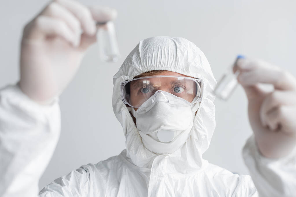 Científico en traje de felpudo mirando vacunas en primer plano borroso  - Foto, Imagen