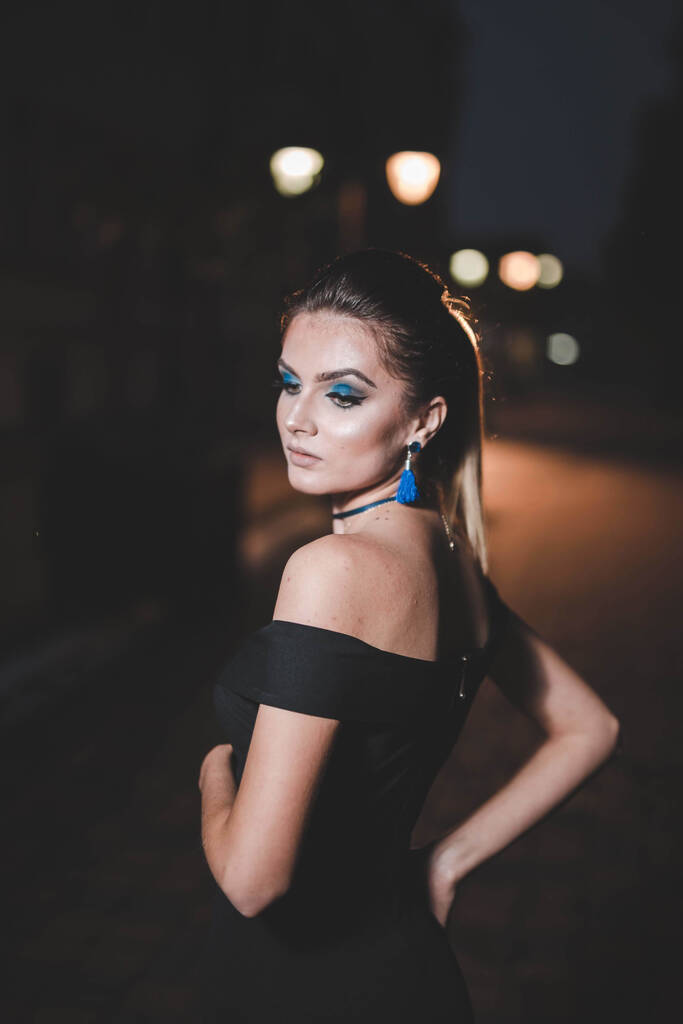 Geceleri sokakta poz veren zarif siyah elbiseli çekici bir kadının dikey fotoğrafı. - Fotoğraf, Görsel
