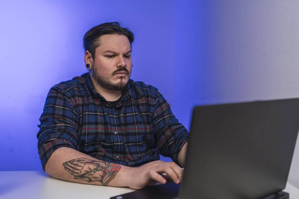 Un uomo barbuto spagnolo con tatuaggi che lavora su un computer portatile - Foto, immagini