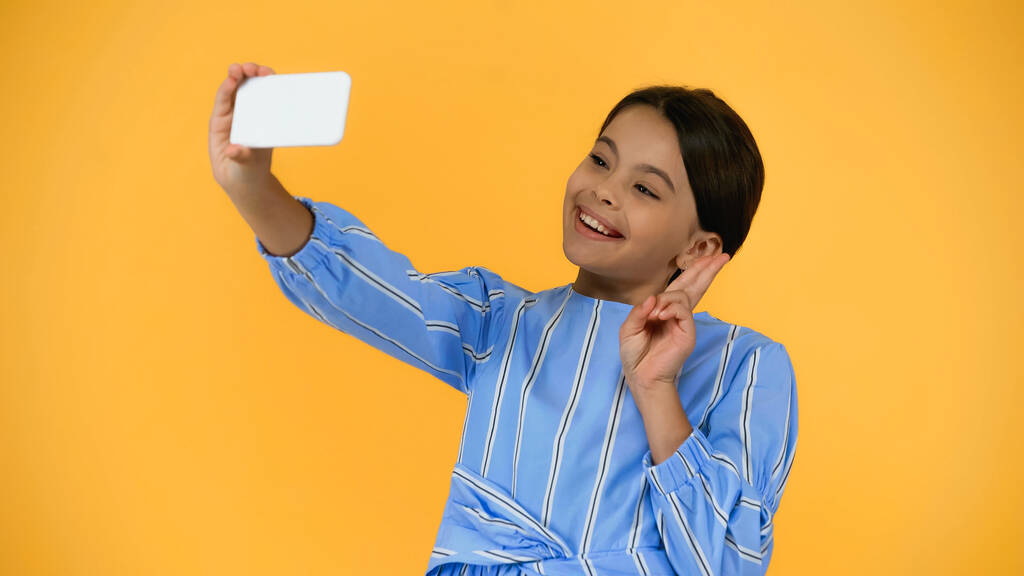 niño preadolescente feliz tomando selfie en el teléfono inteligente aislado en amarillo - Foto, imagen