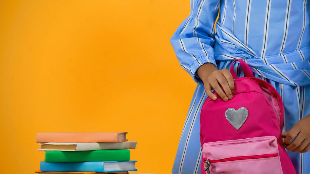 vue recadrée de l'écolière tenant un sac à dos près de livres isolés sur jaune - Photo, image