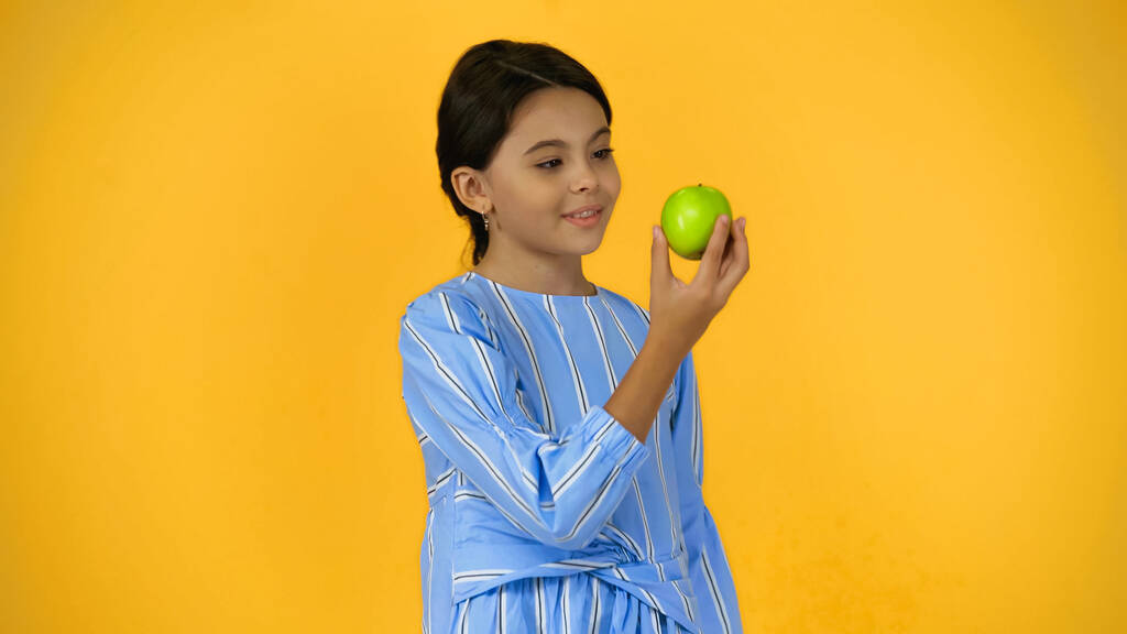 χαρούμενο παιδί που κρατά το πράσινο μήλο απομονωμένο στο κίτρινο - Φωτογραφία, εικόνα