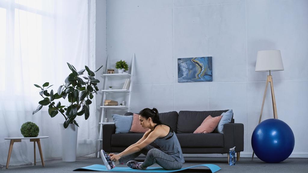 mujer joven en ropa deportiva haciendo ejercicio en la alfombra de fitness en casa  - Foto, Imagen