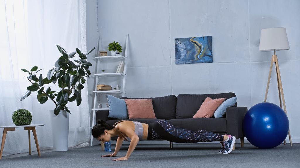 jonge vrouw in sportkleding doen plank oefening thuis  - Foto, afbeelding