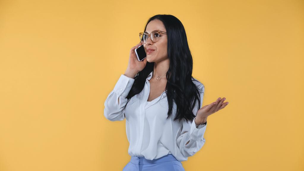 усміхнена бізнес-леді жестикулює під час розмови на мобільному телефоні ізольовано на жовтому
 - Фото, зображення