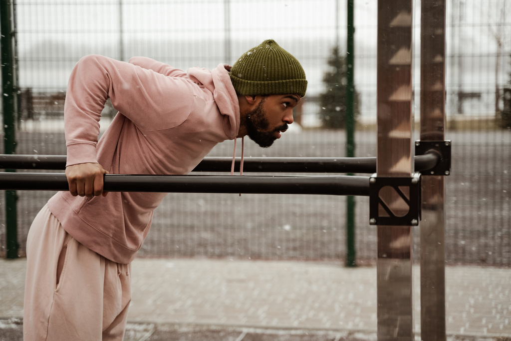 boční pohled na africký americký atlet cvičit na crossbars na stadionu venku - Fotografie, Obrázek