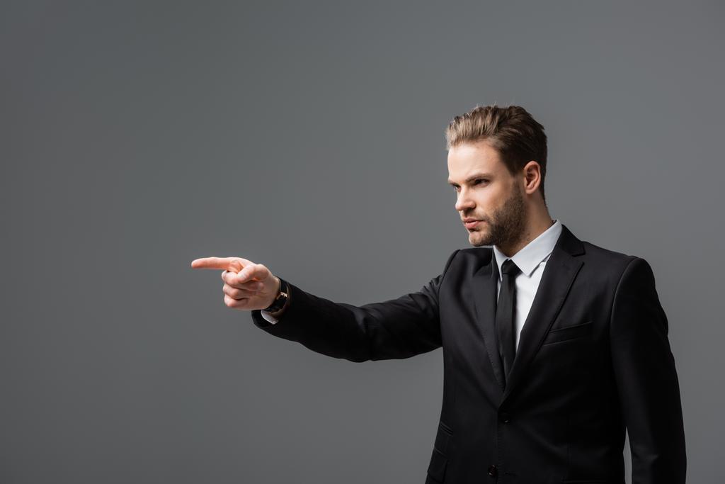 serious businessman looking away and pointing with finger isolated on grey - Photo, Image