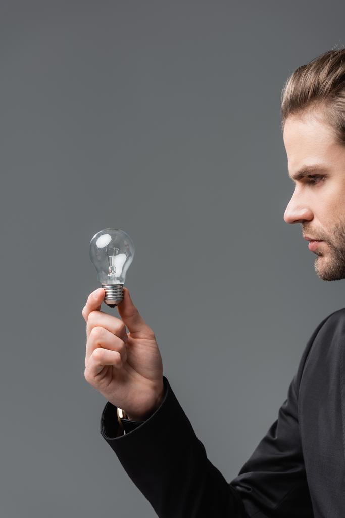 young businessman holding light bulb isolated on grey - Photo, Image